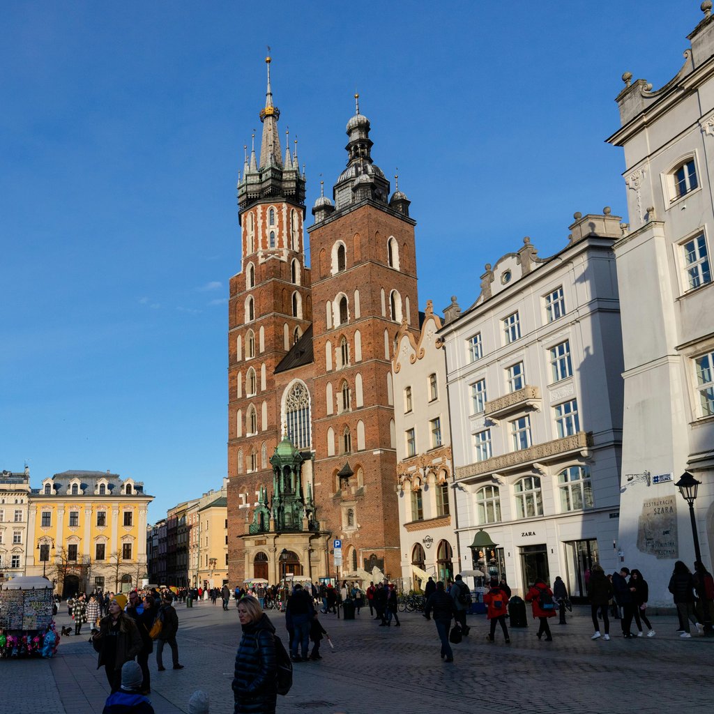 Daytime view of St. Mary's Basilica in Krakow's Main Market Square, under clear blue skies.