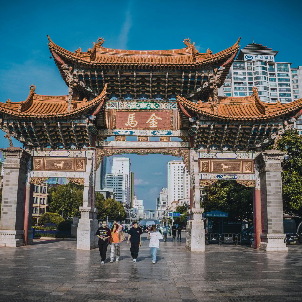Traditional Chinese archway against Kunming city backdrop, attracting tourists.