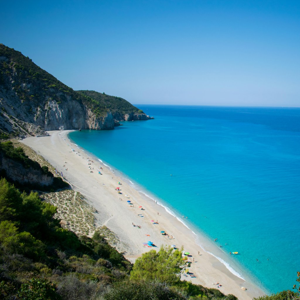 Stunning aerial view of the turquoise waters and sandy beach of Lefkada, Greece, with lush cliffs and a serene atmosphere.