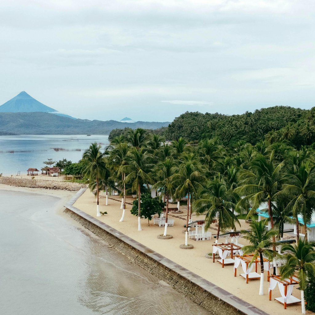Aerial view capturing the scenic beauty of Mayon Volcano and the tropical coastline in Legazpi City, Philippines.