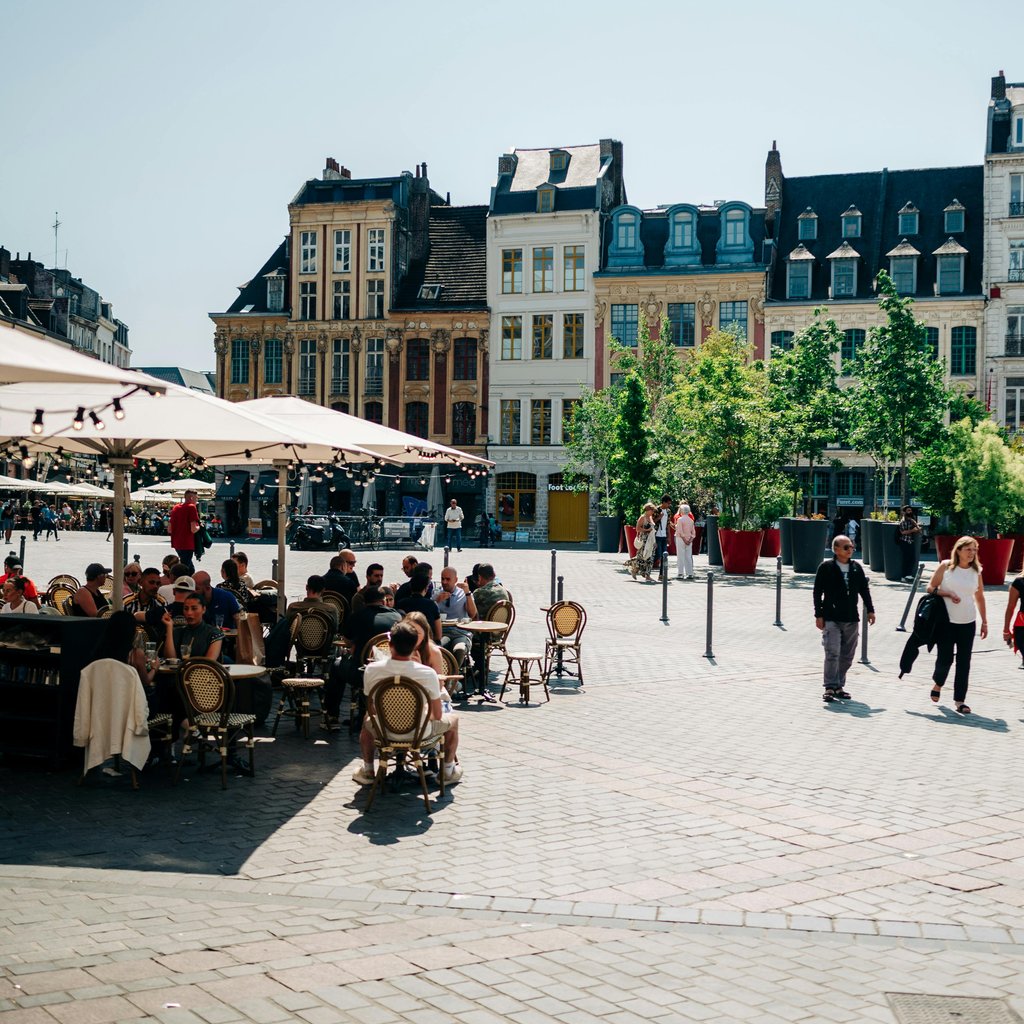 Sunny day in Lille's Old Town Square with people enjoying outdoor cafes under clear blue skies.