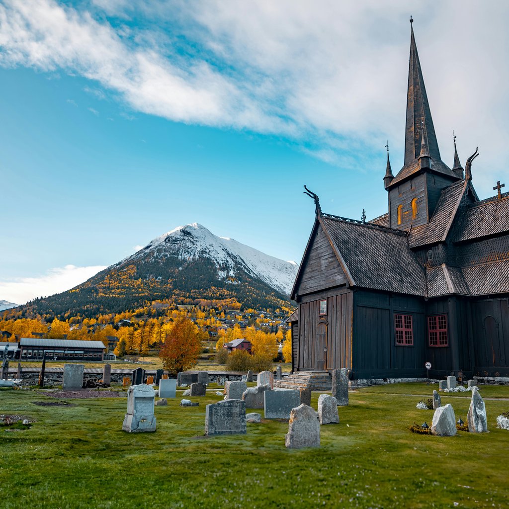 Lom Stave Church with cemetery and mountains in fall, Fossbergom, Norway.