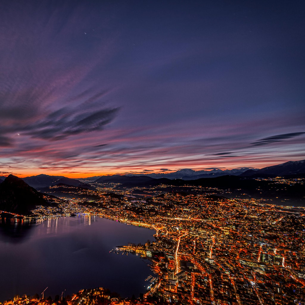 Mesmerizing aerial shot of Lugano city lights reflecting on the lake at twilight.