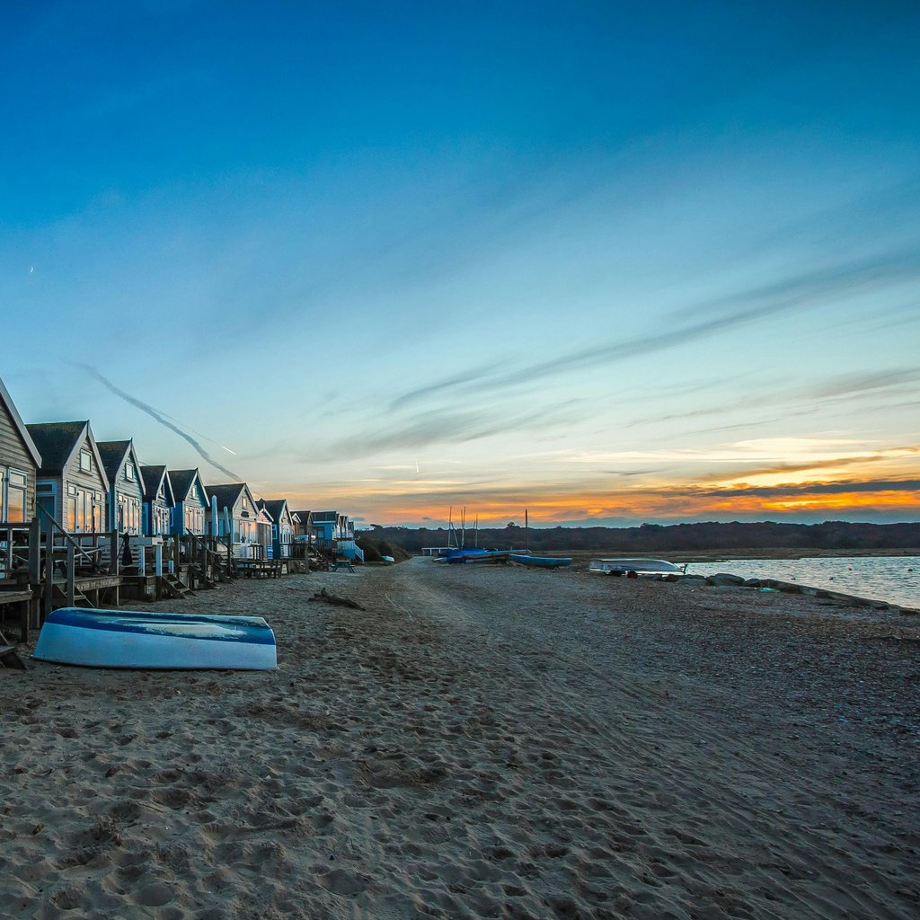Charming beachfront cabins overlook a serene beach and calm waters at dusk, perfect for a tranquil vacation.