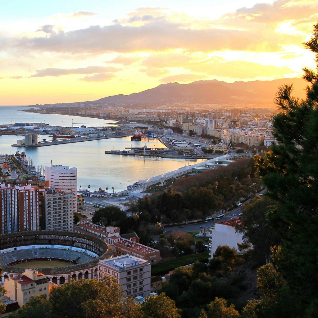 Captivating aerial view of Málaga at sunset, showcasing the port and iconic bullring, with mountains in the background.