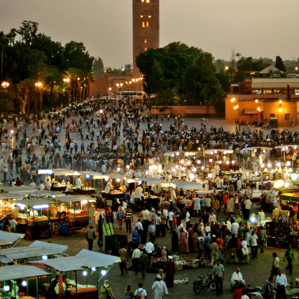 Evening view of bustling Jemaa El-Fnaa market square in Marrakech, Morocco, illuminated with vibrant lights.