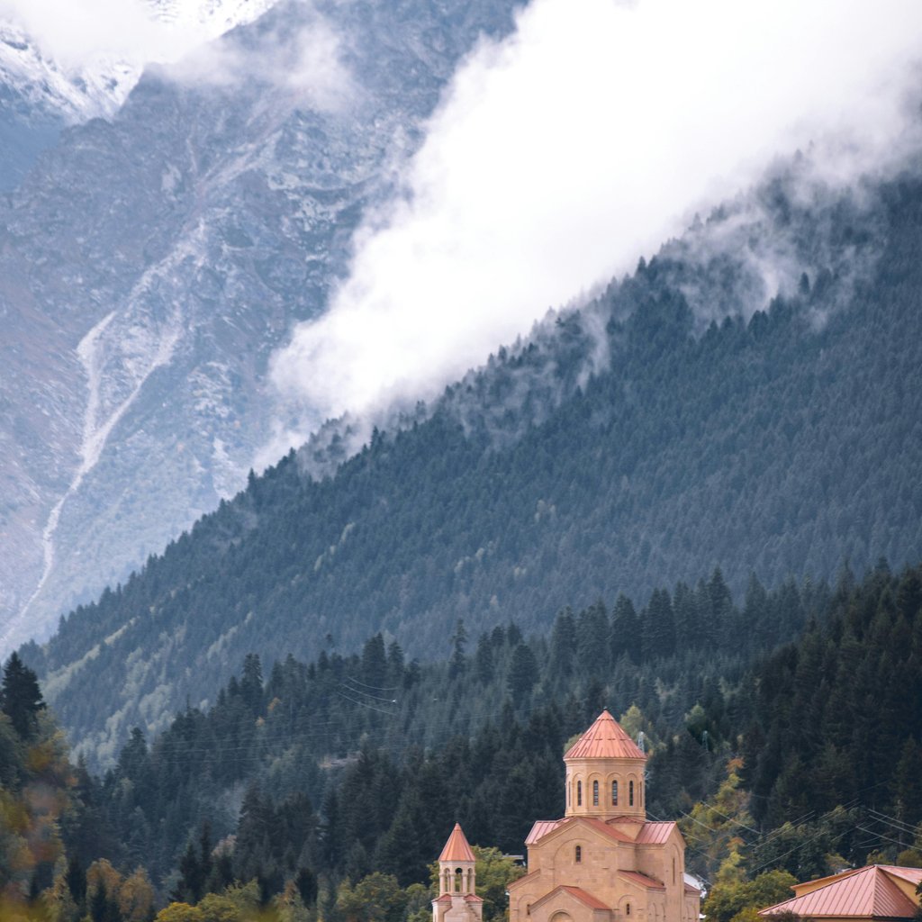 View of a church in Mestia with misty mountains and fog in the Svaneti region.