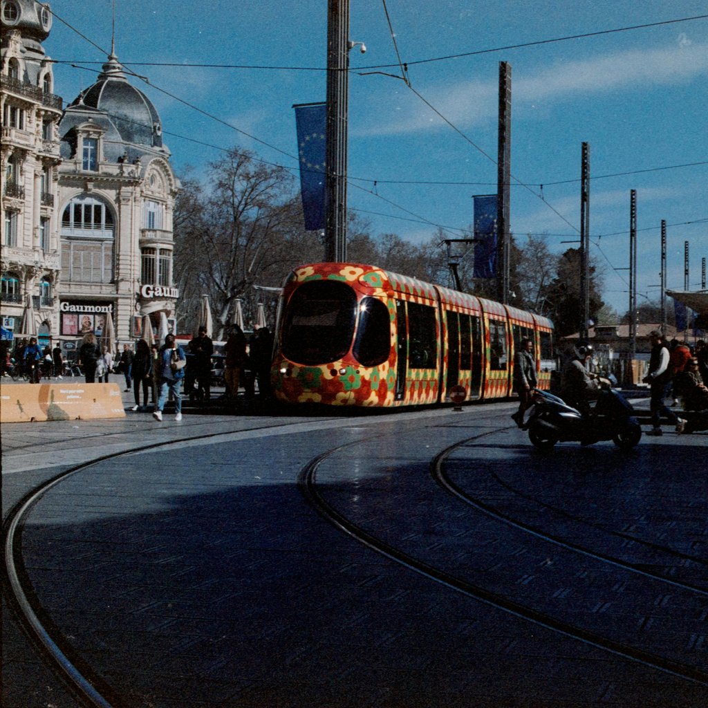 Colorful tram passing through a bustling street in Montpellier, France.