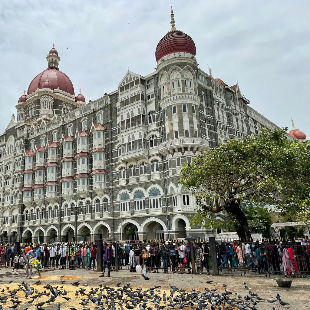 Iconic Taj Mahal Palace Hotel in Mumbai with a bustling crowd and pigeons in the foreground.