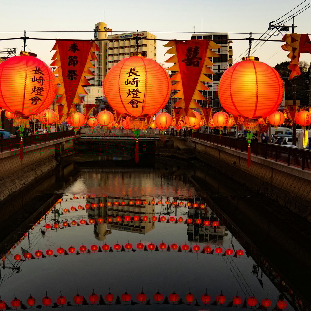 Brightly lit lanterns line a canal in Nagasaki, Japan, reflecting vibrantly in the calm water.
