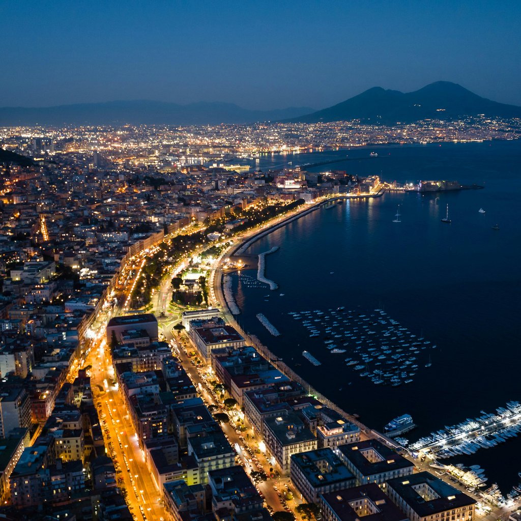 Stunning aerial view of Naples cityscape and harbor, illuminated at night with Mount Vesuvius in the background.