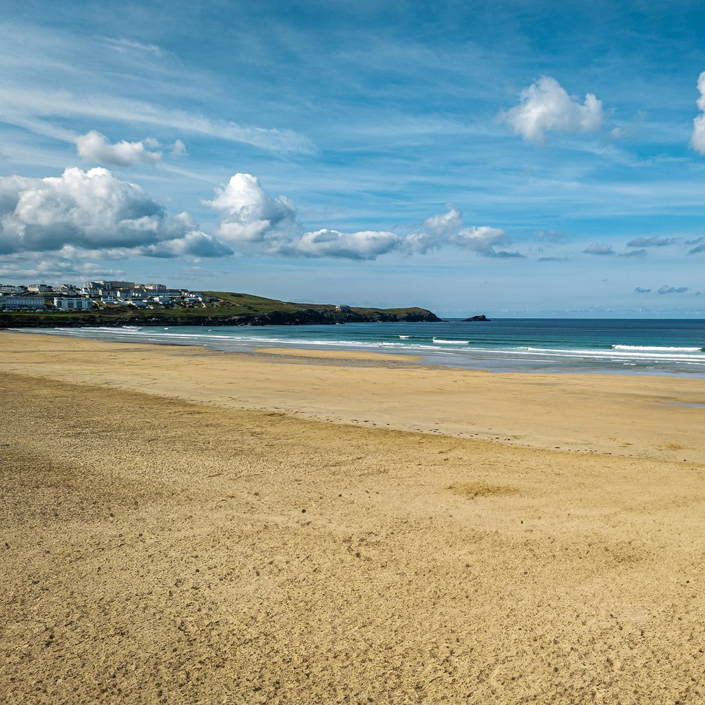 Golden sandy beach in Newquay with blue skies and calm sea, perfect for tourism and relaxation.