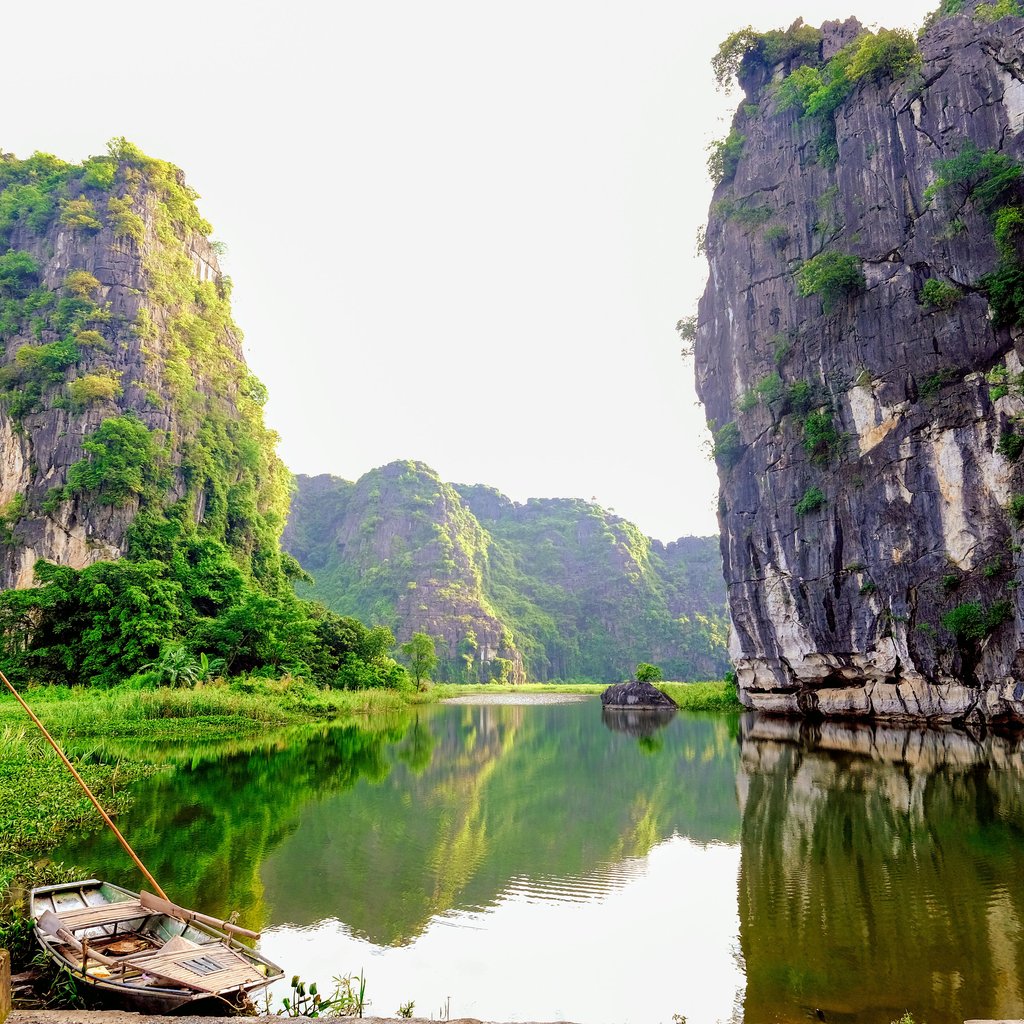 Tranquil scene of Ninh Binh's limestone cliffs and serene water reflection, featuring a traditional rowboat.