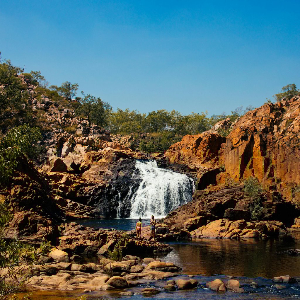Picturesque view of rapid foamy cascade falling from rough stiff cliff slope into small pond in peaceful highlands on sunny day