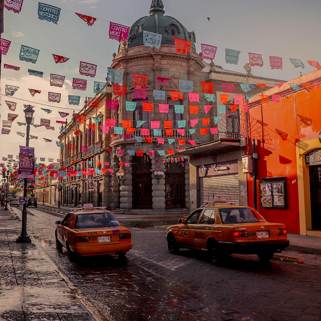 Colorful papel picado decorates the streets of Oaxaca, Mexico, with taxis passing by.