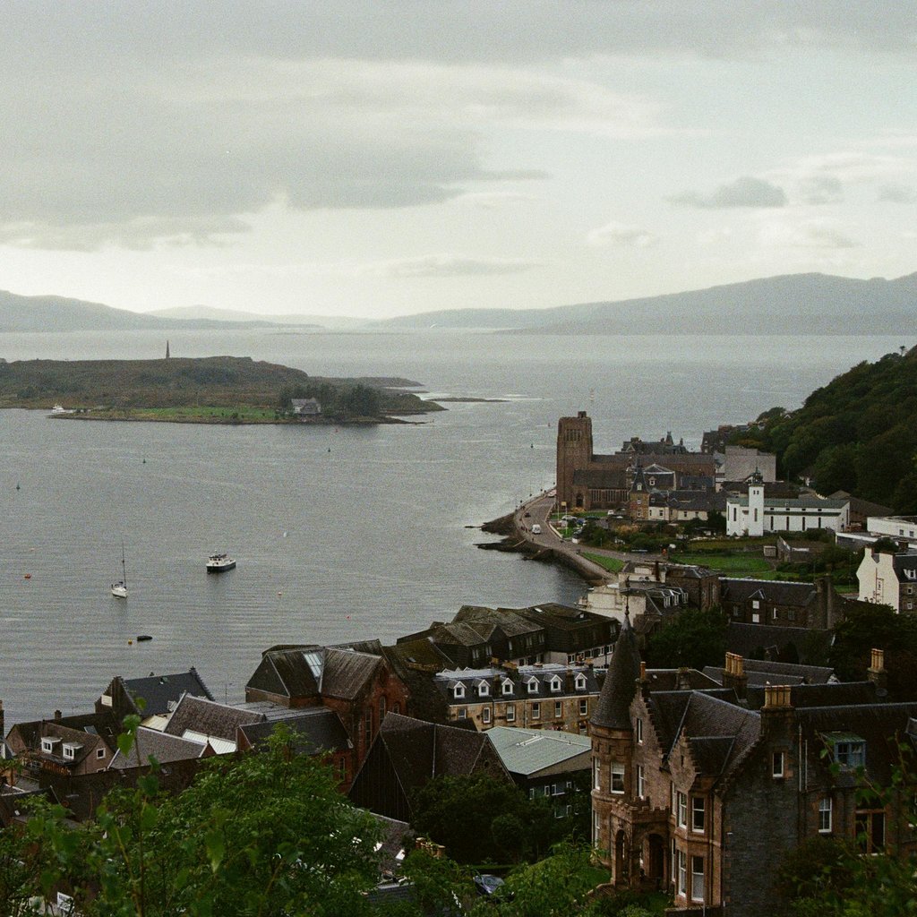 A picturesque view of Oban Bay, Scotland, capturing boats, historic buildings, and distant mountains.