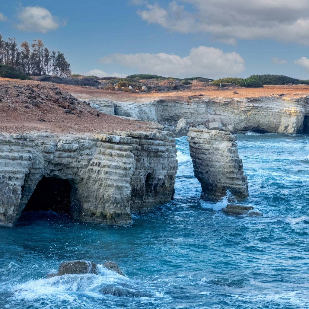 Explore the stunning sea caves and blue waters along the rocky coast of Paphos, Cyprus.