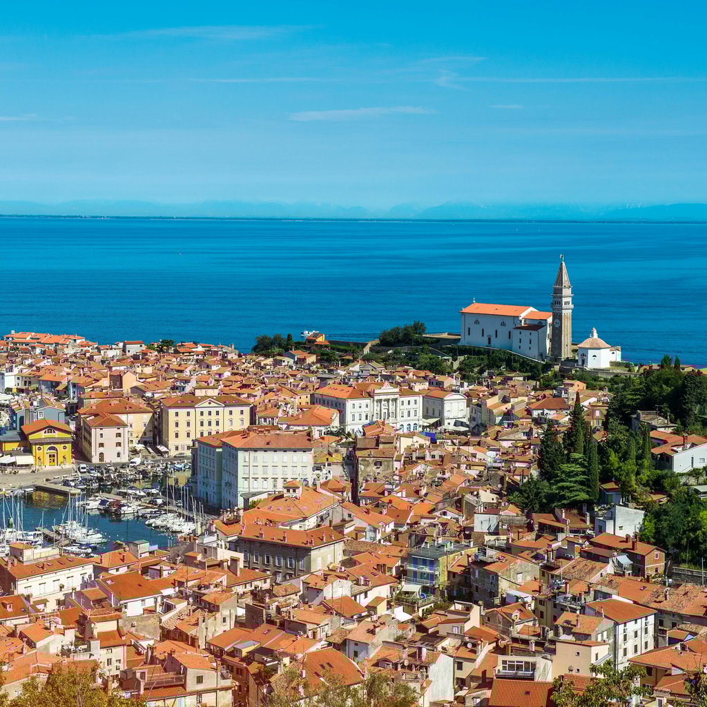 A stunning aerial view of Piran, Slovenia, showcasing the picturesque harbor and historic architecture under a bright summer sky.