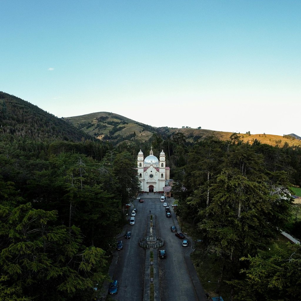 A stunning aerial photo capturing a church surrounded by lush hills and forests.