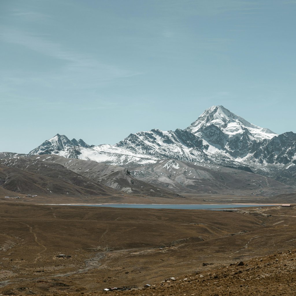 Explore the magnificent snowcapped Huayna Potosi mountain and serene lake in Bolivia's vast landscape.