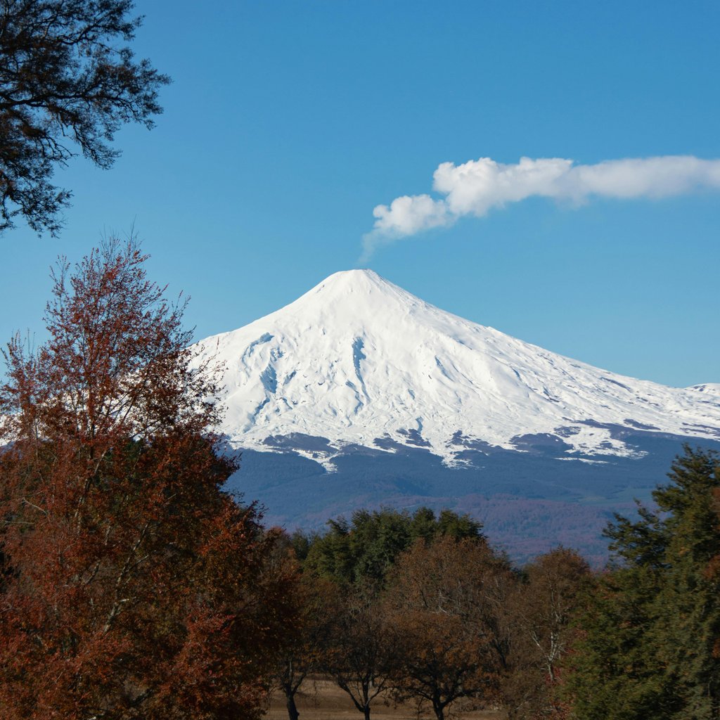 Stunning view of Villarrica Volcano with snow cap and smoke against a vibrant blue sky.