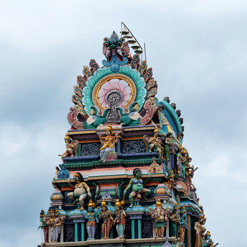 Detailed view of a vibrant temple gopuram against a cloudy sky in Puducherry, India.