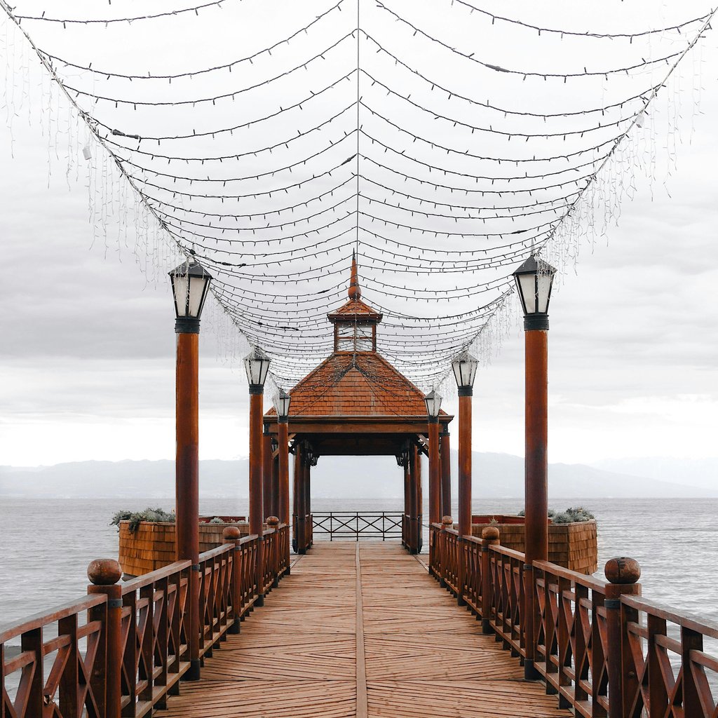 Charming wooden pier with canopy lights on Lake Llanquihue, Puerto Varas, Chile, showcasing symmetry and scenic views.