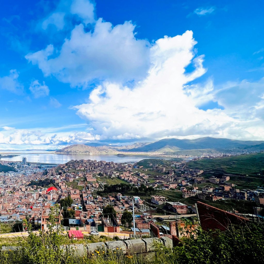 Captivating aerial view of Puno, Peru, with stunning Lake Titicaca in the background under a bright blue sky.
