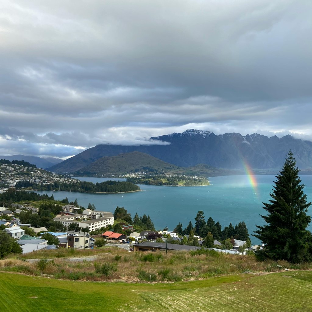 Aerial view of Queenstown, New Zealand with Lake Wakatipu, mountains, and a rainbow.