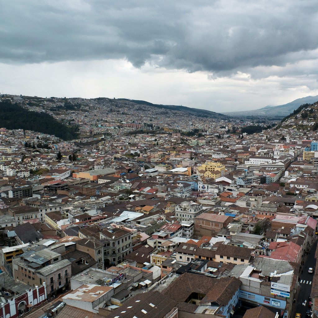 Expansive aerial view of Quito's historic cityscape with cloudy skies, featuring scenic hills and urban density.
