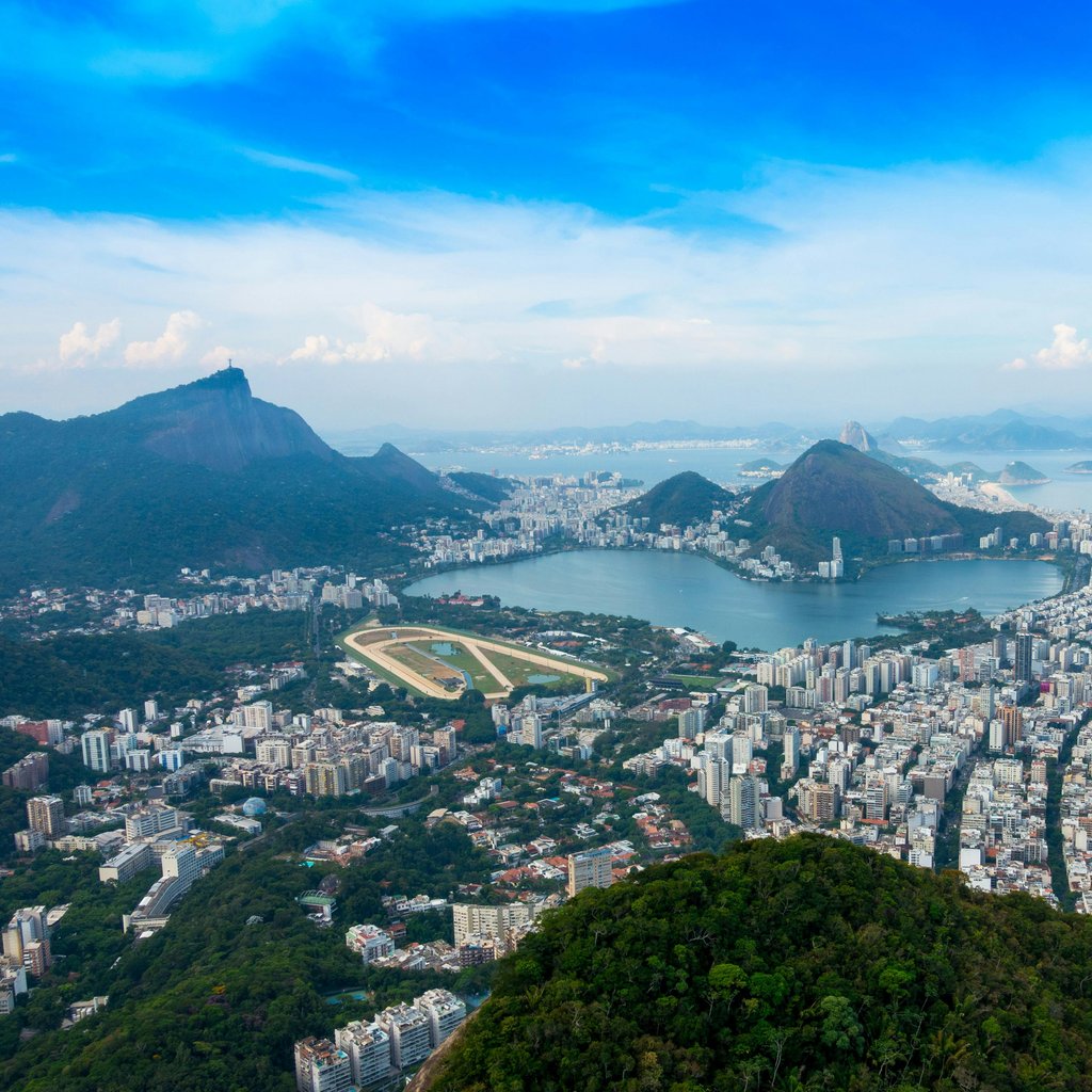 Panoramic aerial view of Rio de Janeiro's coastline, iconic landmarks, and lush mountains.