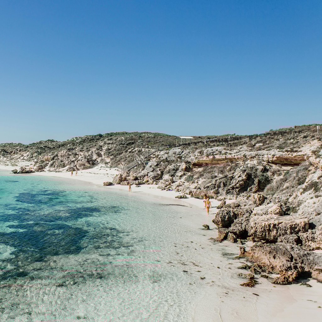 Beautiful sandy beach with clear turquoise water and rocky shoreline under a bright blue sky.