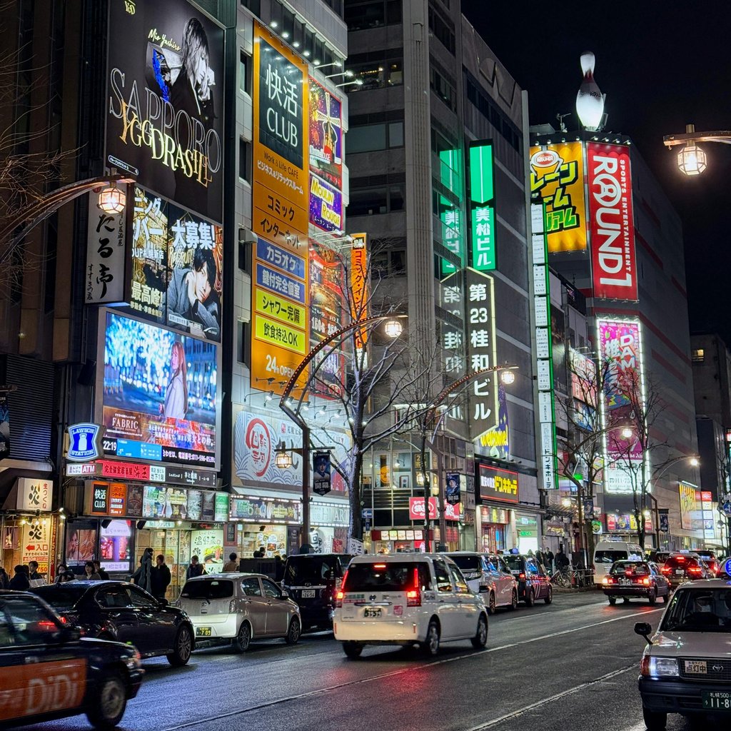 Bustling nightlife in Sapporo with illuminated signage and traffic, showcasing vibrant urban culture.