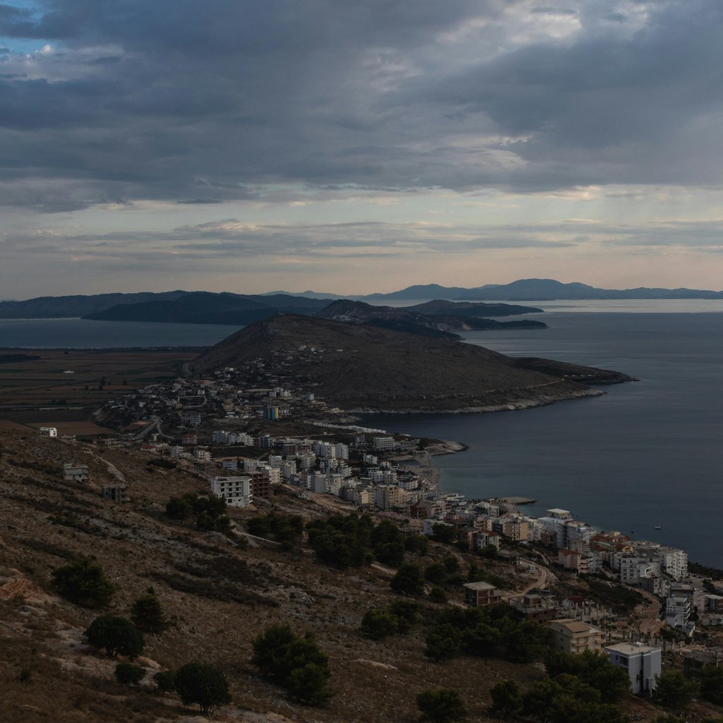 Serene coastal landscape of Saranda, Albania with hills and islands under a cloudy sky.