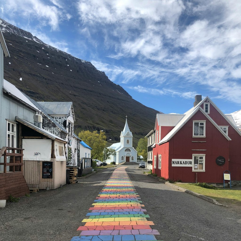 Picturesque view of Seydisfjordur's rainbow pathway leading to the iconic white church under a blue sky.