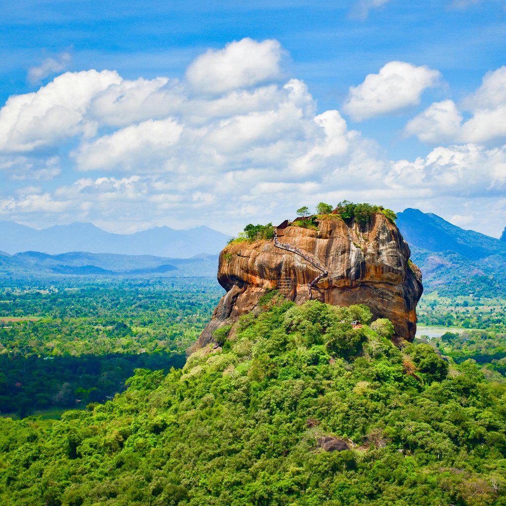 Explore the iconic Sigiriya Lion Rock surrounded by lush greenery and vibrant blue skies in Sri Lanka.