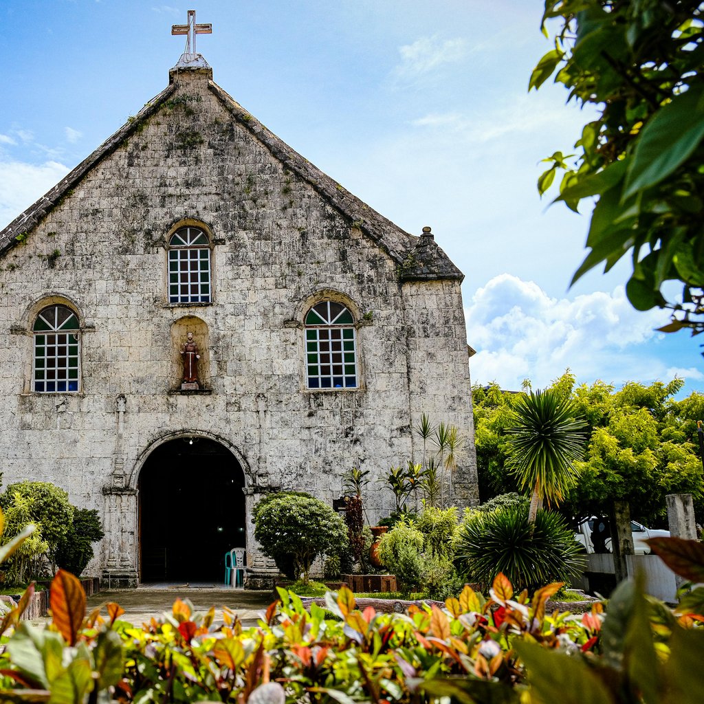 Stone facade of St. Francis de Assisi Church with lush flora and blue sky.