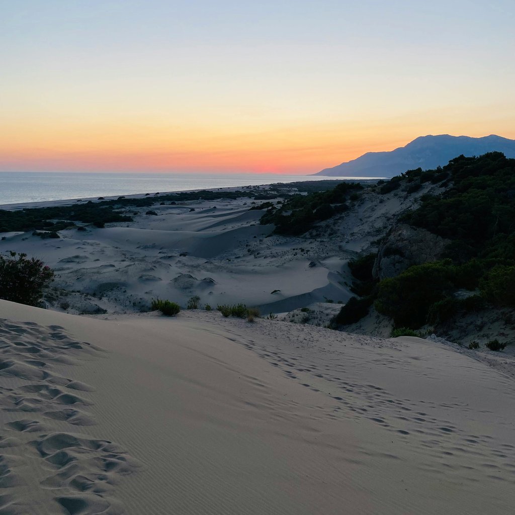 A serene landscape of coastal dunes at sunset with mountain backdrop.