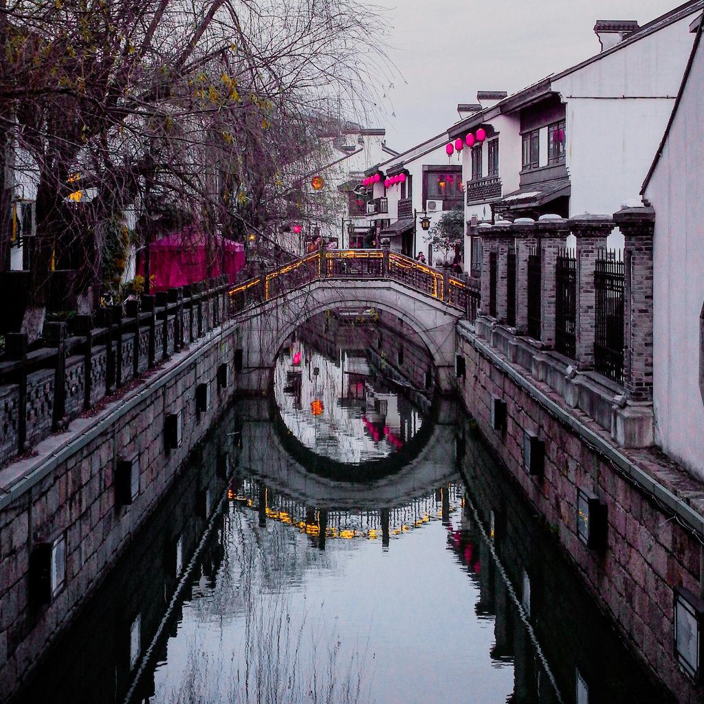 Picturesque moon bridge and canal reflection in Suzhou at dusk depicting urban tranquility.