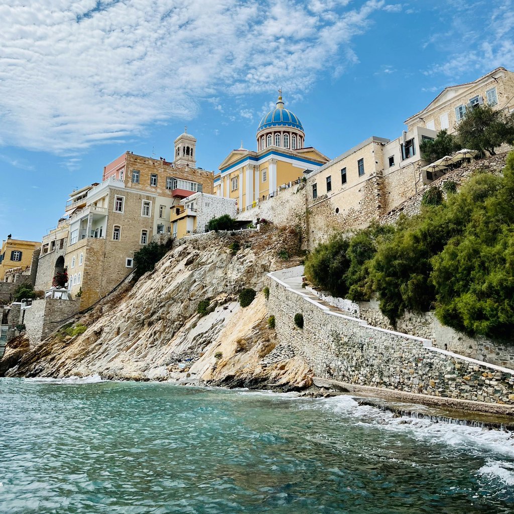 Breathtaking coastal view of Syros, Greece featuring a striking church with blue dome and colorful buildings.