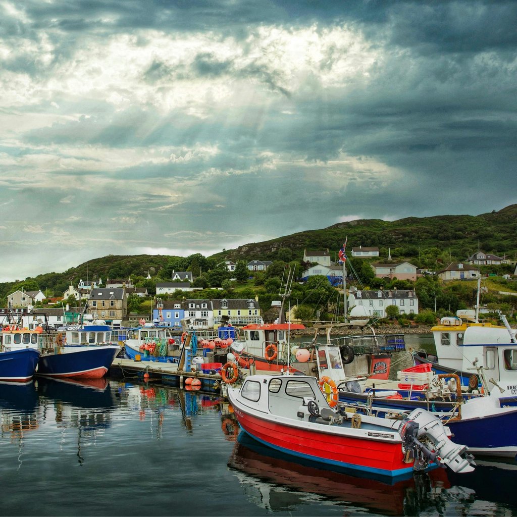 Picturesque fishing boats docked in Tarbert harbor, Scotland, under dramatic skies.