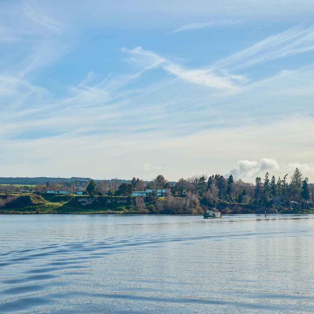 Tranquil view of Lake Taupō with a boat and distant shoreline under a bright blue sky.