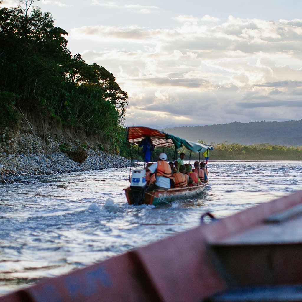Tourists enjoy a scenic riverboat ride along the Napo River in Tena, Ecuador, surrounded by lush greenery and mountains.