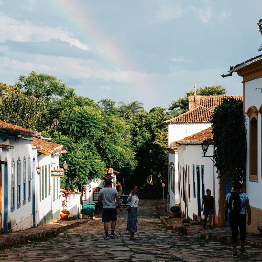 Scenic view of people walking on a cobblestone street in Tiradentes with colonial buildings and a rainbow.