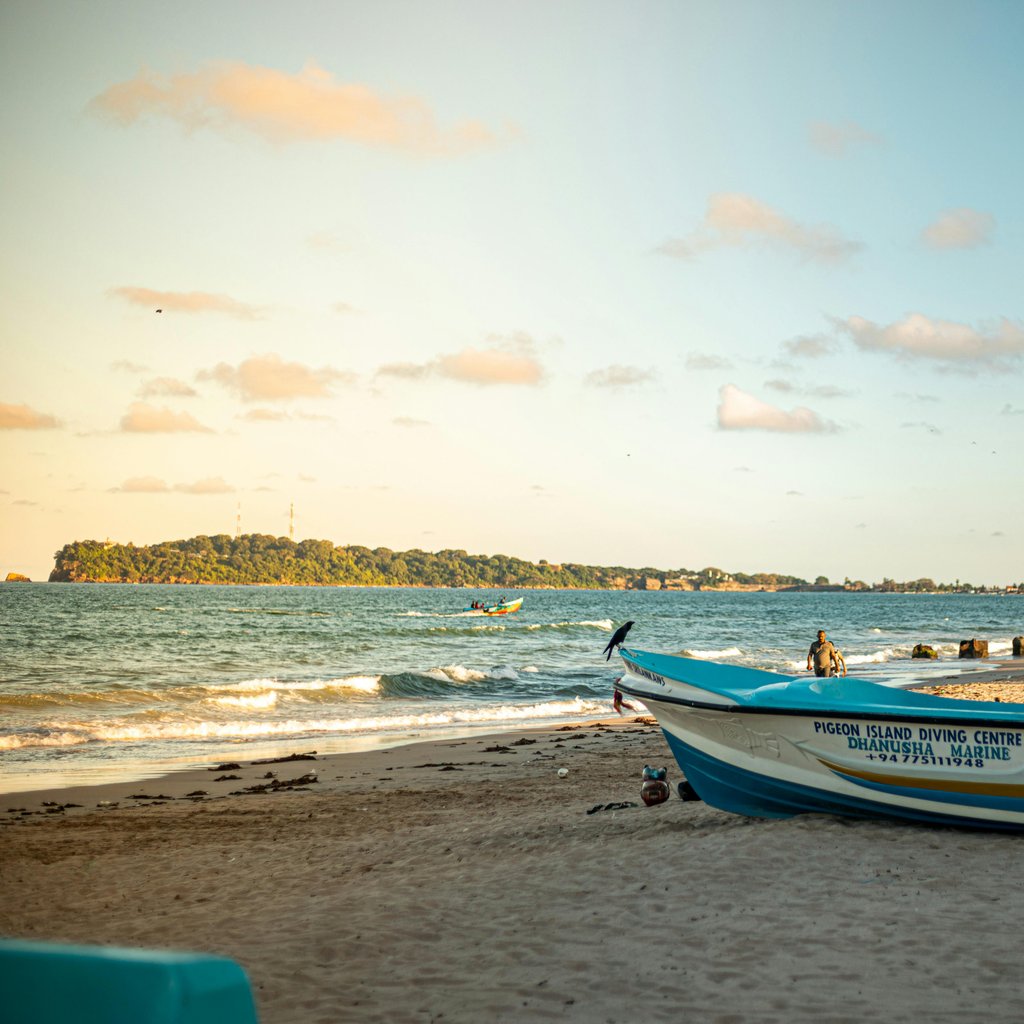 A tranquil beach in Trincomalee, Sri Lanka with boats and people enjoying the serene scenery in the evening light.
