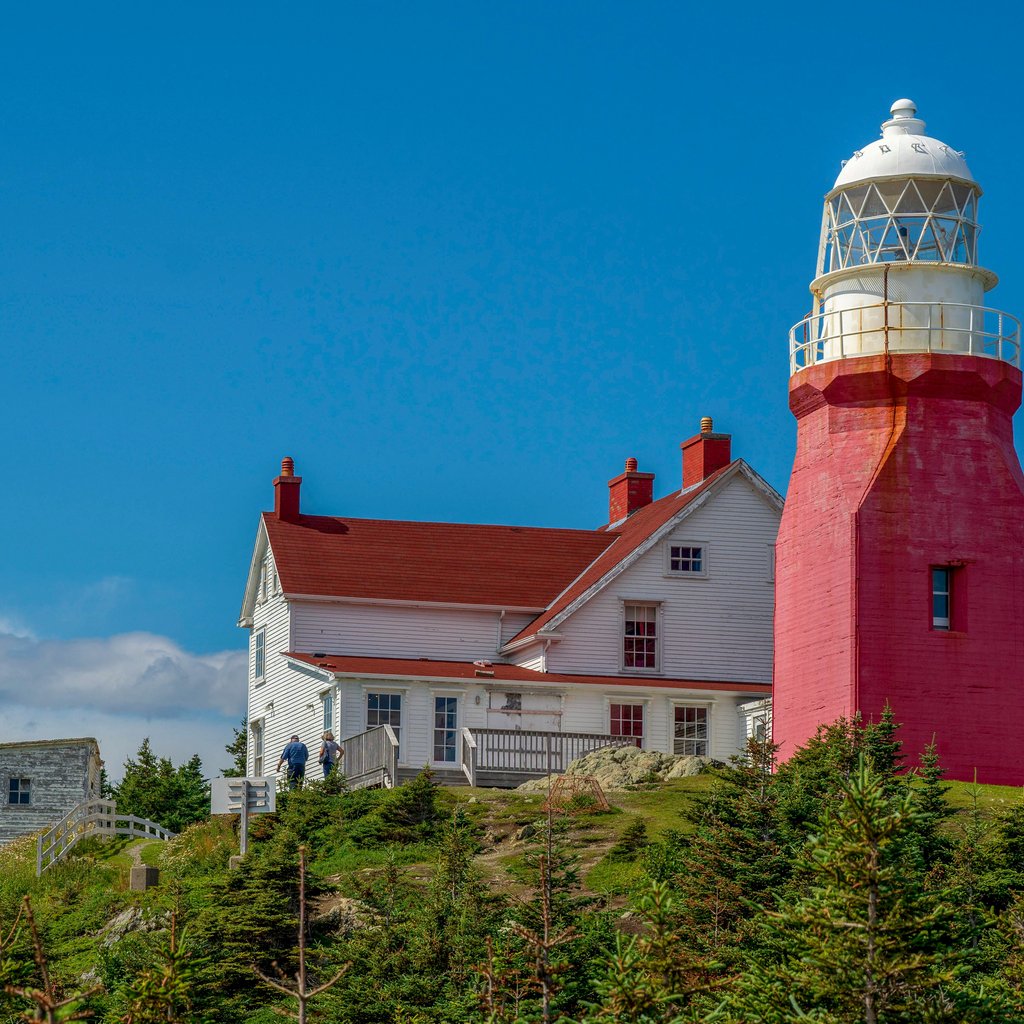 Long Point Lighthouse in Newfoundland under a clear blue sky during summer.