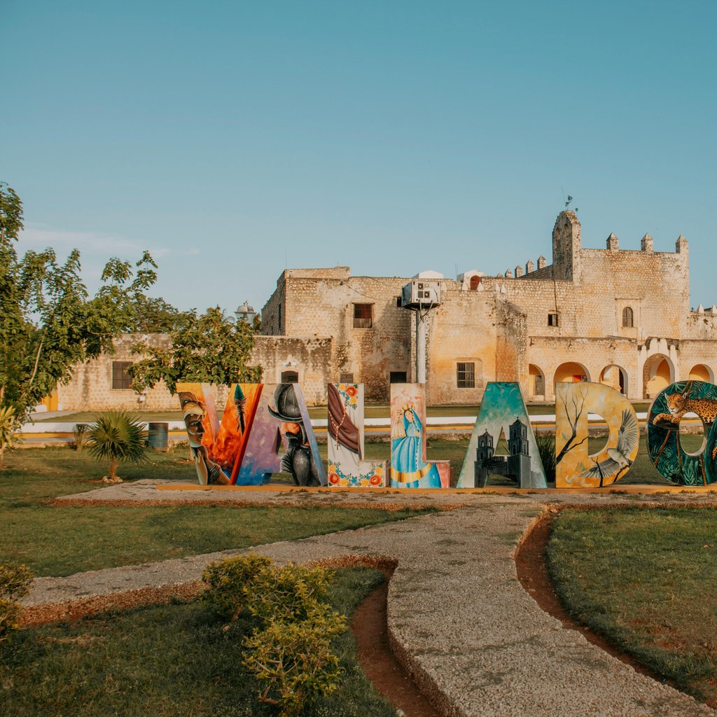 Vibrant Valladolid letters in front of a historic convent in Mexico, surrounded by greenery.