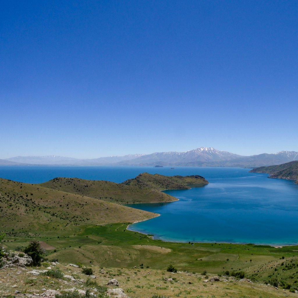 Stunning aerial view of Lake Van, with vibrant turquoise waters surrounded by green hills and distant mountains in Türkiye.