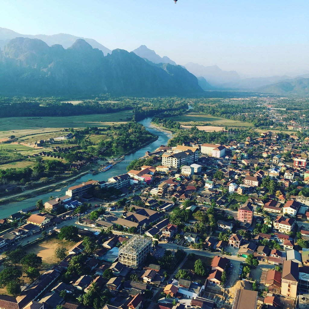 Discover the breathtaking aerial view of Vang Vieng, Laos, with a hot air balloon soaring above the town.