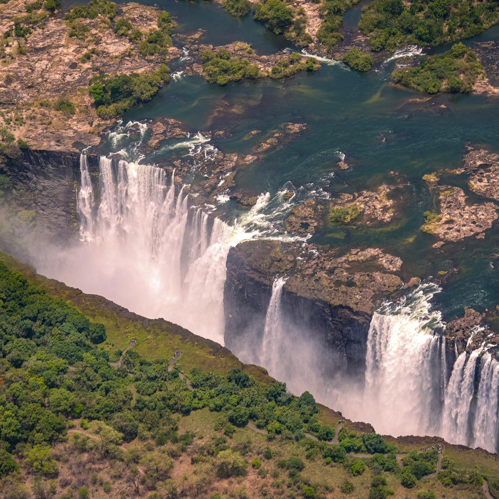 Breathtaking aerial view of Victoria Falls surrounded by lush greenery during summer day.